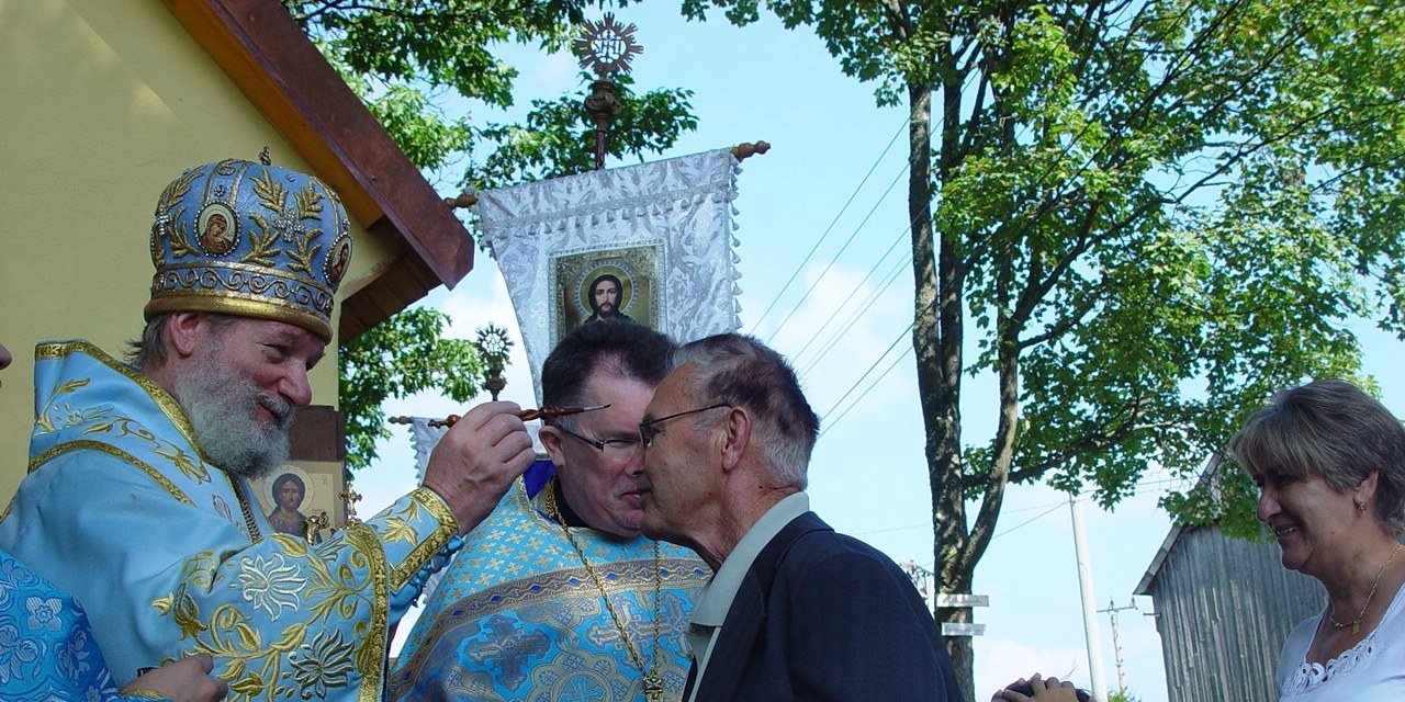 Vysvěcení kaple na Tachovsku — vladyka žehná členům obce, v pozadí korouhev s ikonou Krista